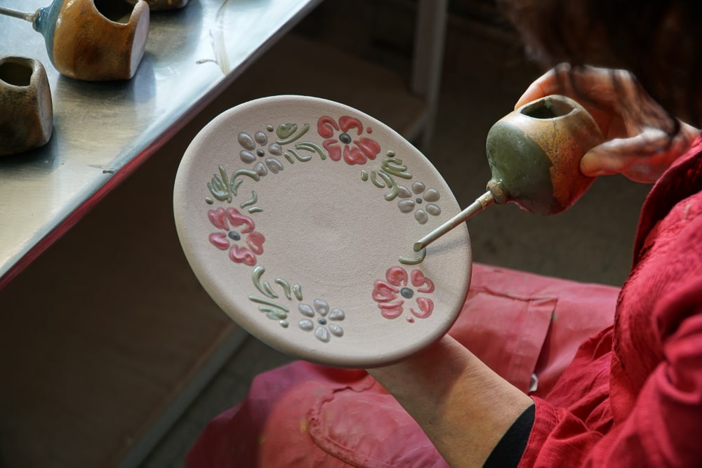 Décoratrice qui réalise une décoration sur une assiette en poterie.